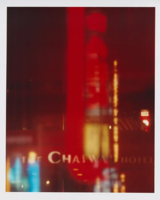 Blurred image of the Chaiwai Hotel at night, with a tall red neon sign and reflections of city lights in the windows. The scene is abstract.