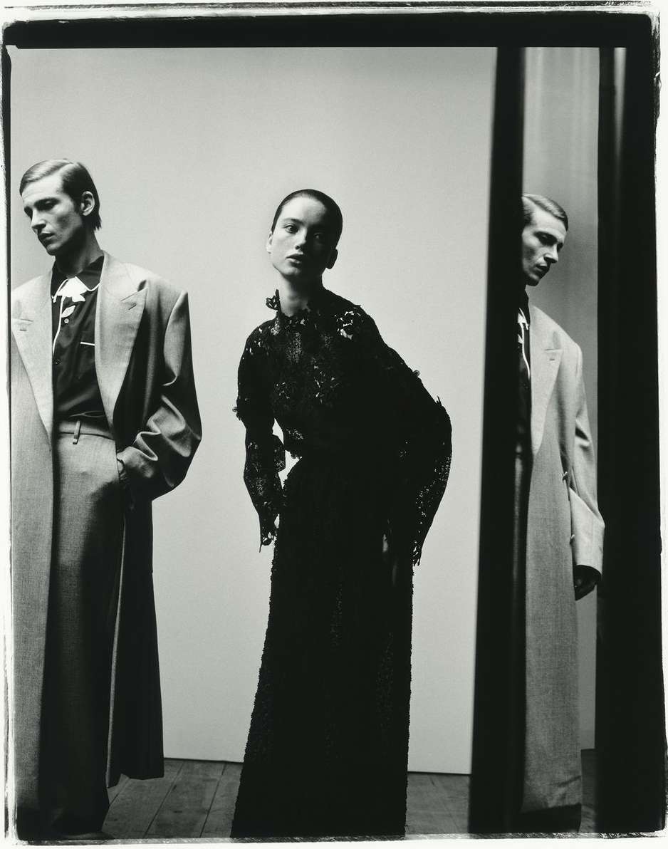 Fashion shot featuring two men in suits and an adult woman in an evening gown, captured in a high-fashion studio setting with neutral backdrop.