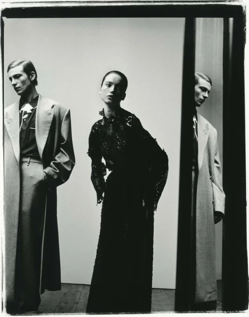 Fashion shot featuring two men in suits and an adult woman in an evening gown, captured in a high-fashion studio setting with neutral backdrop.