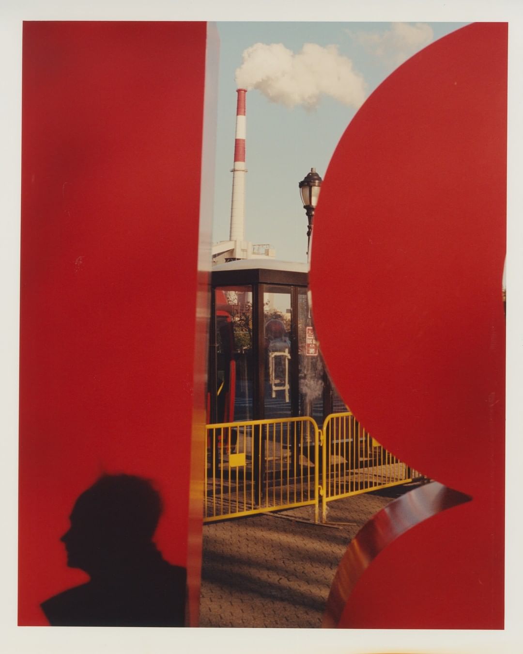 Artistic urban photo of a silhouetted head, red geometric shapes, and a distant smokestack, creating depth and visual interest in the city.