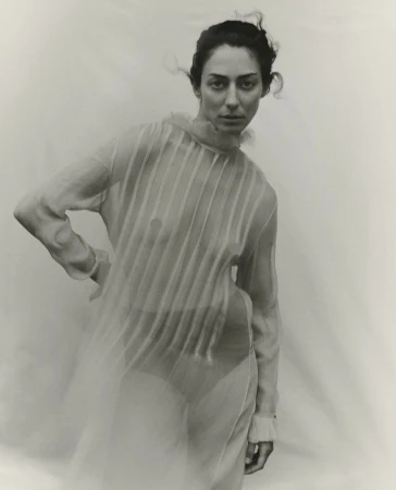 Adult woman in sheer dress poses in photo studio against a neutral background in a fashion photography style, monochromatic filter.