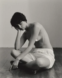 Seated woman with short dark hair wearing white boxer shorts on a dark wooden floor in Paris by Denis Boulze