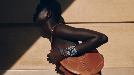 Model in profile carrying a leather handbag against a wall with harsh sunlight and shadow cast across the scene