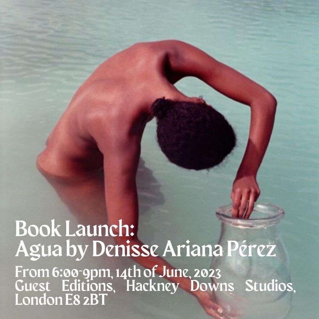 Person stands in shallow water holding a glass vase in front of a promotional poster for a book launch in London in June 2023.
