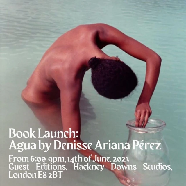 Person stands in shallow water holding a glass vase in front of a promotional poster for a book launch in London in June 2023.