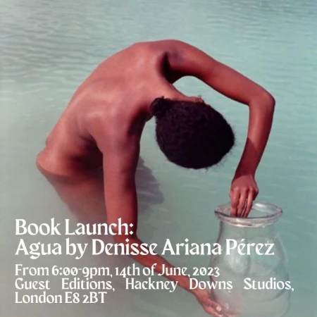 Person stands in shallow water holding a glass vase in front of a promotional poster for a book launch in London in June 2023.