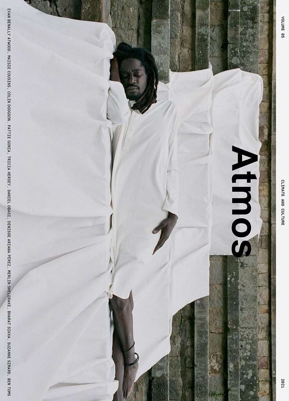 Magazine cover featuring a Black man with dreadlocks in a white outfit, resting on a white cloth with a stone step background.