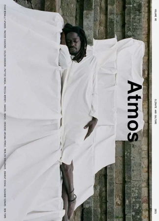 Magazine cover featuring a Black man with dreadlocks in a white outfit, resting on a white cloth with a stone step background.