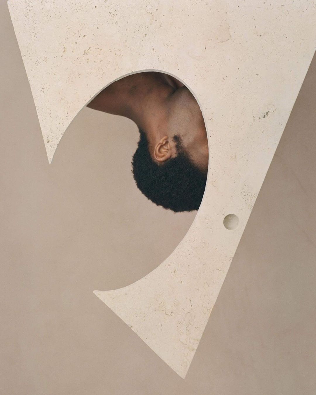 Abstract art with a close-up of an African-American man's head and neck framed by a large, triangular, beige architectural cutout.