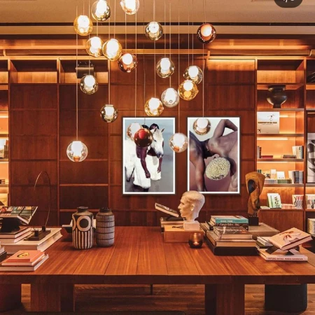 Stylish interior featuring a wooden table with books, vases, and sculptures, framed by artwork and decorative lighting with warm tones and bookshelves.