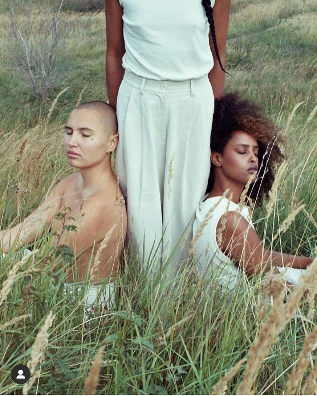 Three people sitting amidst tall meadow grass, captured in a portrait by photographer Denisse Ariana Perez in Amsterdam.