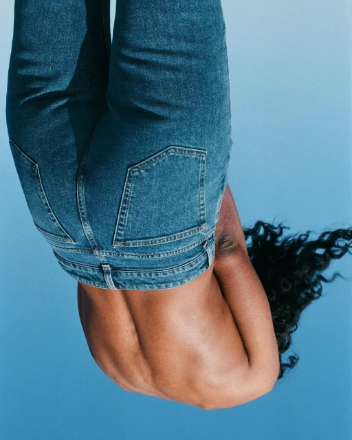 An adult female with dark curly hair and blue jeans is seen from the back against a clear, bright blue sky background.