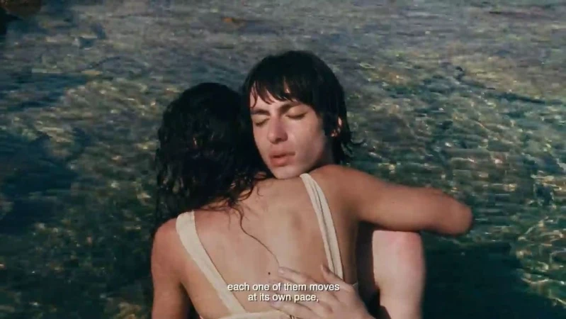 Two people embracing in shallow coastal water with subtitle text overlay at the bottom