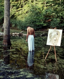 Shirtless man in white trousers standing in a shallow swamp with an easel and canvas by Denisse Ariana Perez