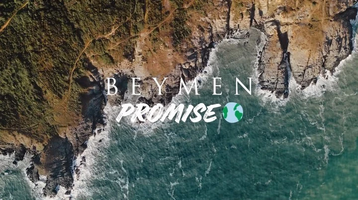 Aerial view of the coastline with turquoise water, rocky cliffs, and a sandy beach. Text overlay: Beymen Promise.
