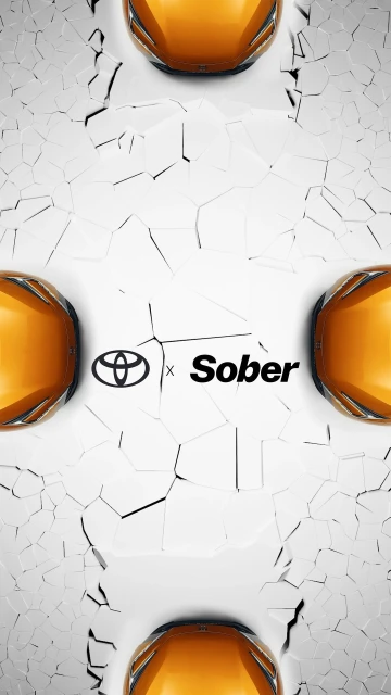 Close-up of three orange Toyota cars against a cracked white surface with the Toyota and Sober logos prominently displayed in the center.