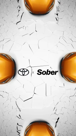 Close-up of three orange Toyota cars against a cracked white surface with the Toyota and Sober logos prominently displayed in the center.