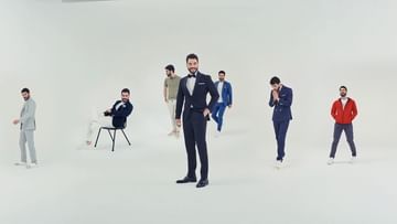 Group of men in suits standing in a bright, white photo studio; one man in a dark suit is center-frame, others behind him are blurred.