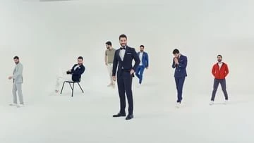 Group of men in suits standing in a bright, white photo studio; one man in a dark suit is center-frame, others behind him are blurred.