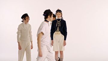 Group of four fashion models in a white studio setting, wearing nautical-inspired white and navy outfits with detailed embellishments.