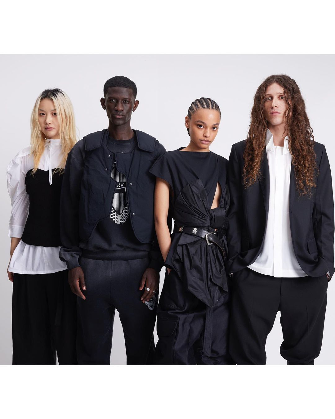 Four diverse fashion models in black-and-white contemporary clothing pose against a white backdrop in a studio setting.