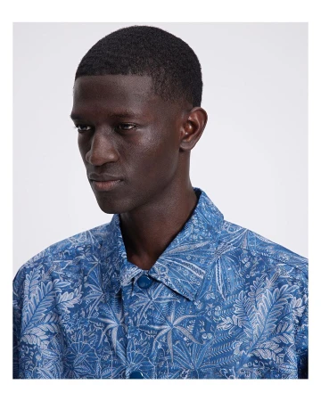 Close-up of a dark-skinned adult male wearing a blue collared shirt with a light gray floral print, facing slightly left.