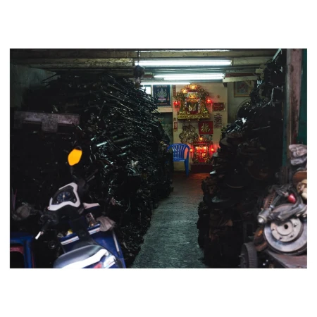 Indoor shot of stacked used motorcycle parts, filling the frame, with a glimpse of a shrine and blue chair in the background.