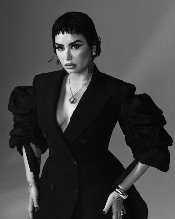 Monochrome portrait of a woman with short dark hair, wearing a tailored double-breasted black blazer with puffed sleeves, and jewelry.