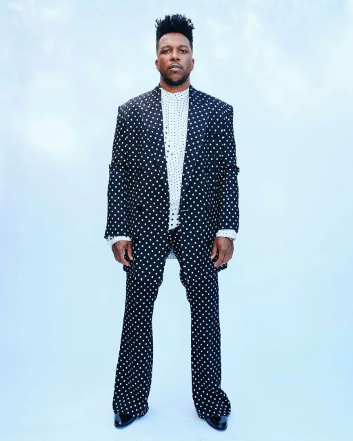 Full shot of adult male wearing a black and white polka dot suit against a light blue background in a studio fashion style.