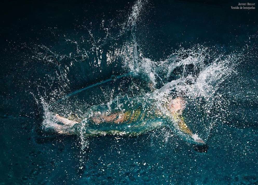 Woman in a dress plunges into deep blue water creating a splash, under studio lighting, photographed at eye-level.
