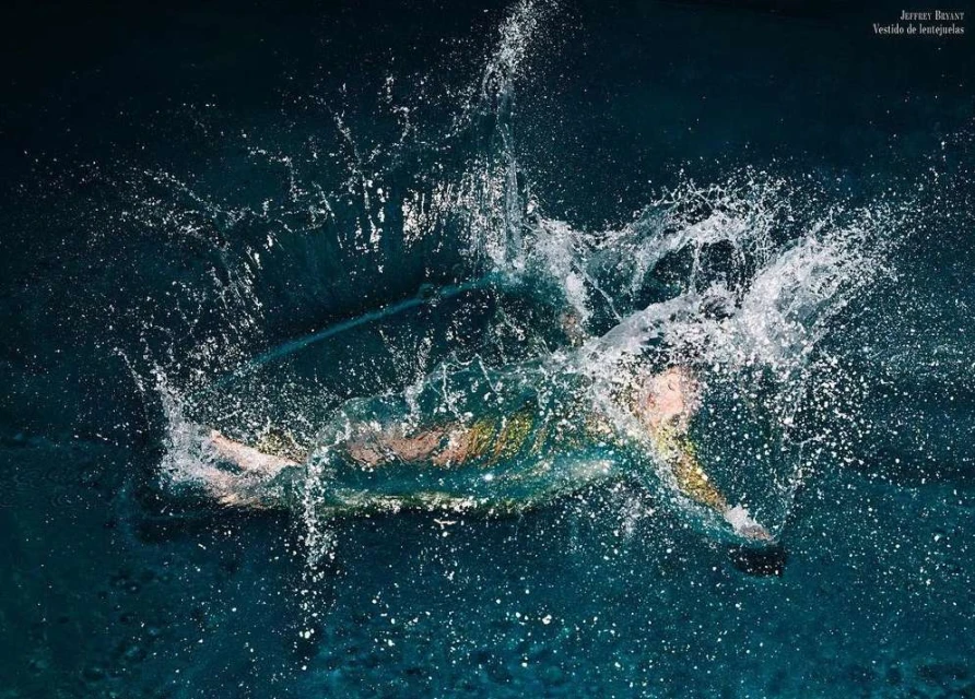 Woman in a dress plunges into deep blue water creating a splash, under studio lighting, photographed at eye-level.