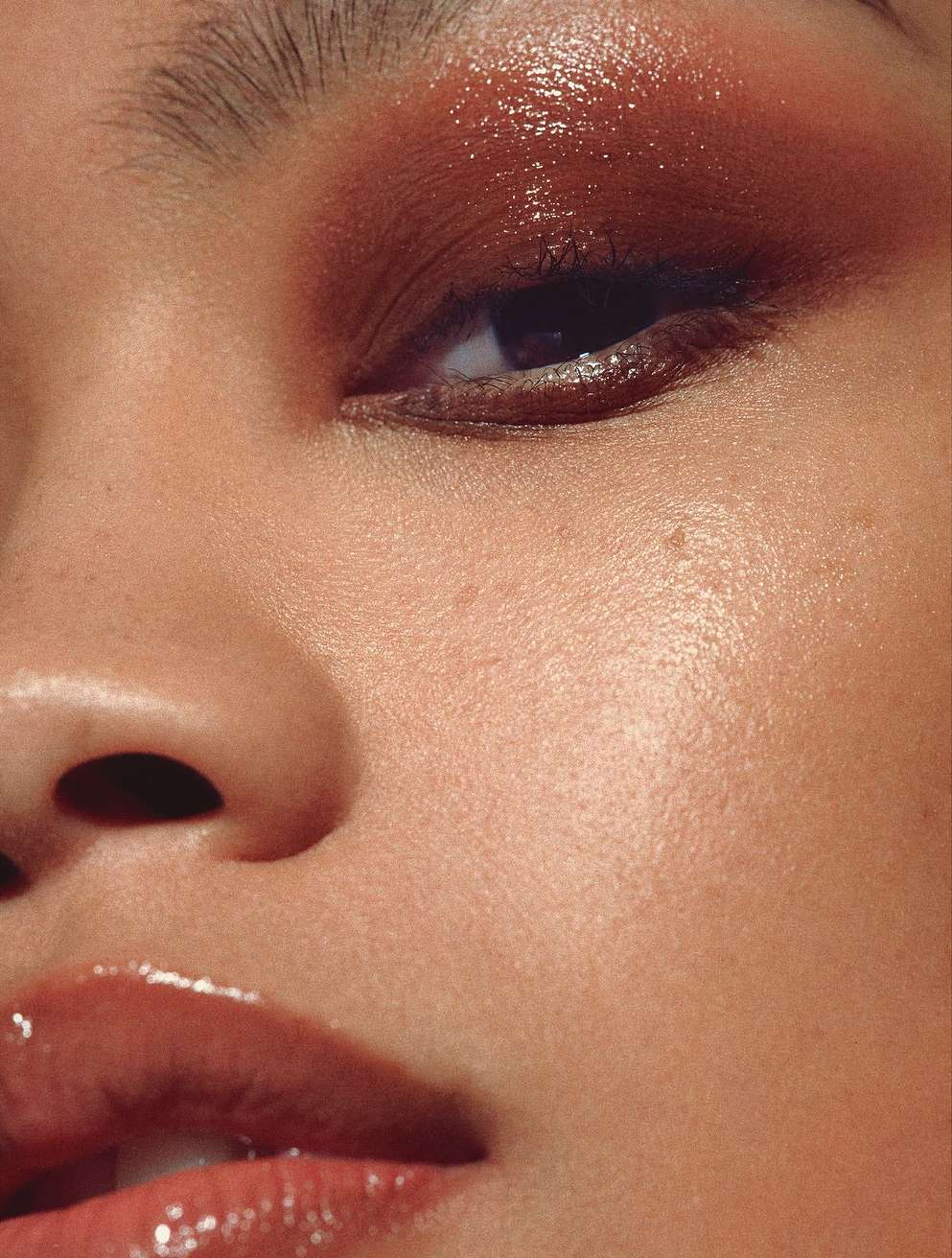 Close-up studio shot of a young woman's face featuring bronze eyeshadow and glossy lips, highlighting beauty and makeup artistry.