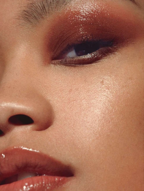 Close-up studio shot of a young woman's face featuring bronze eyeshadow and glossy lips, highlighting beauty and makeup artistry.