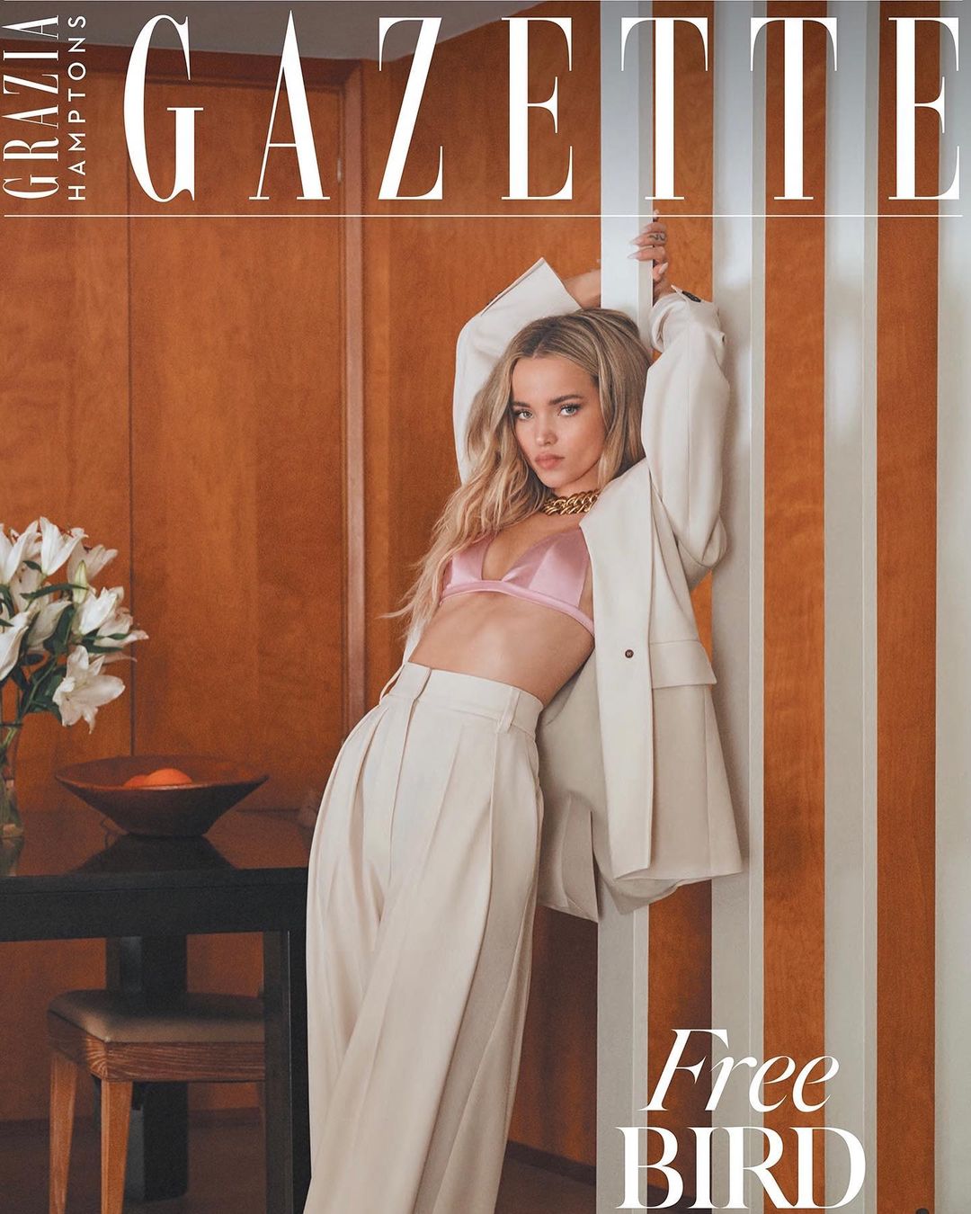 Magazine cover shot of a young adult woman in a pale pink bra, off-white suit, leaning against a wall, with orange and white vertical stripes.