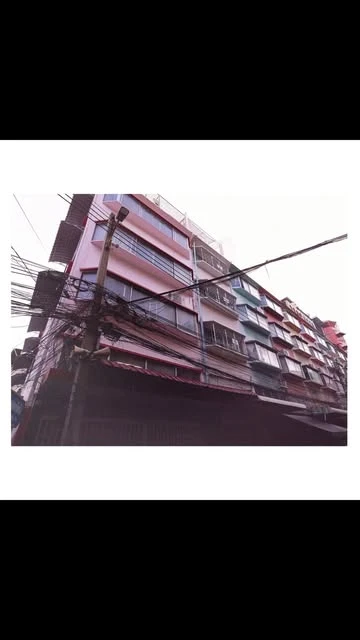 Angled low-angle shot of a multi-story building in an urban environment with electrical wires and architectural details.