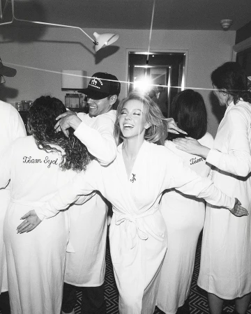 Black and white photo of Sydney Sweeney in a white robe, surrounded by her team in matching robes, celebrating in an indoor setting.