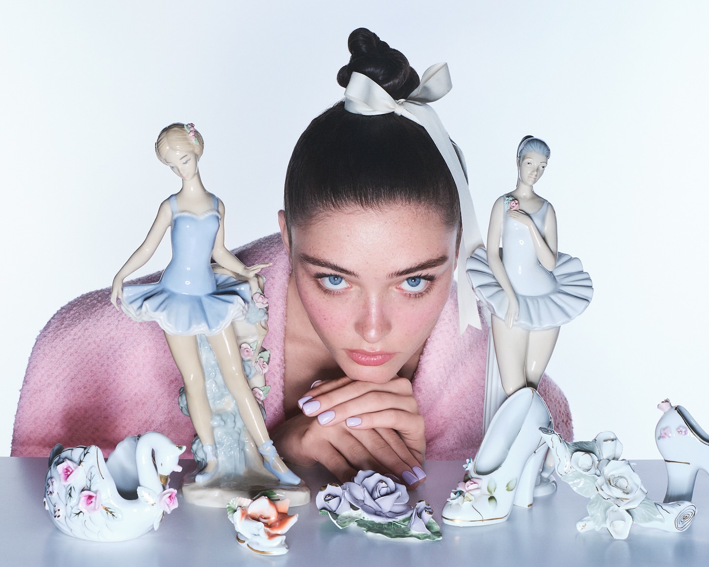 Portrait of a young woman with a high bun and ribbon, surrounded by decorative ballerina figurines and porcelain rose ornaments.