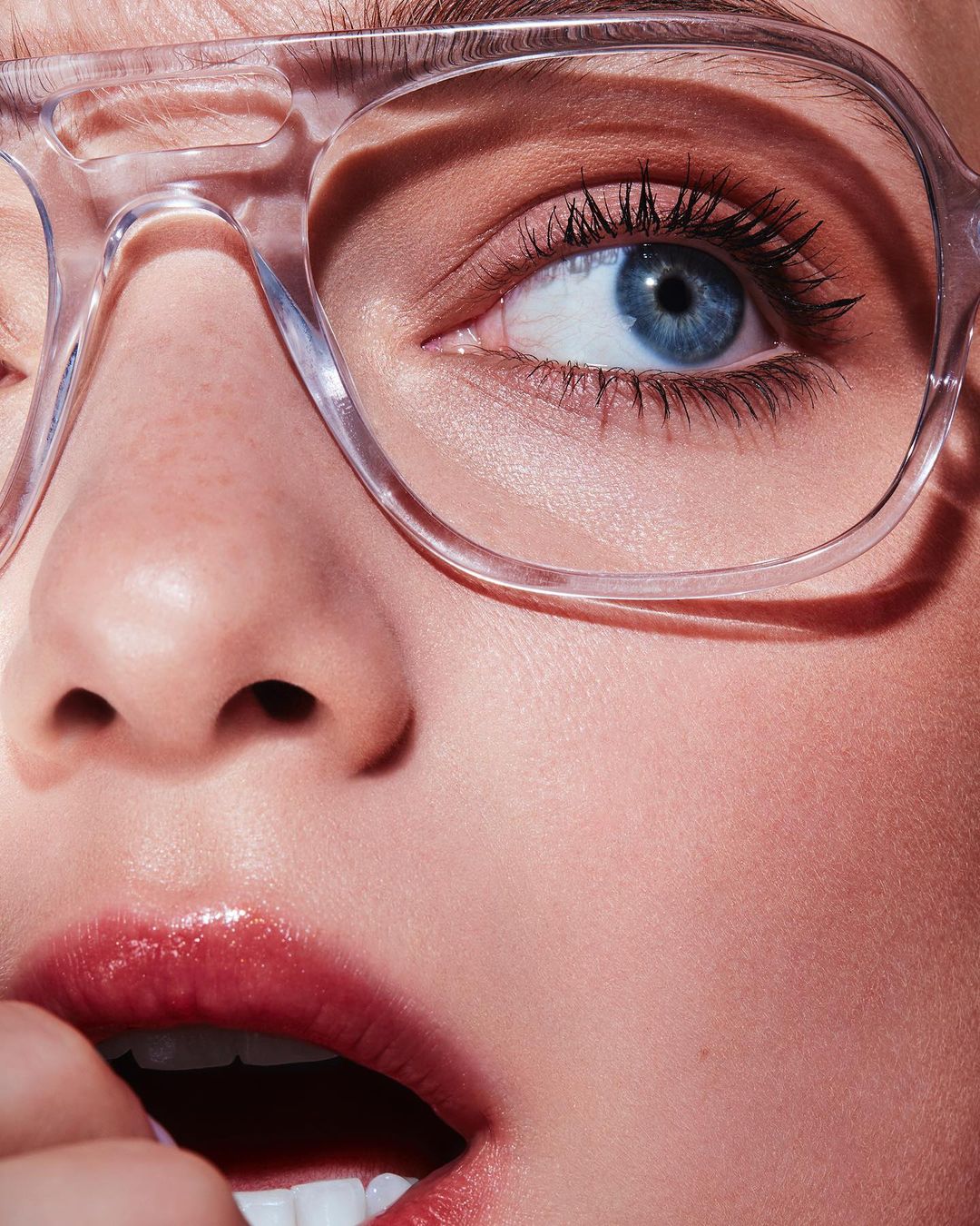 Macro close-up of a fair-skinned woman with blue eyes wearing transparent glasses, illuminated by even lighting showcasing beauty details.