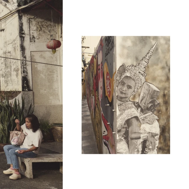 Woman sitting on a stone bench near a building with a street art wall of painted faces in an outdoor urban environment.