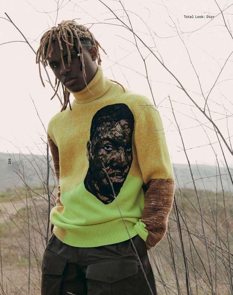 Male model in outdoor fashion editorial wearing yellow turtleneck sweater with a face graphic, and dark green cargo pants.