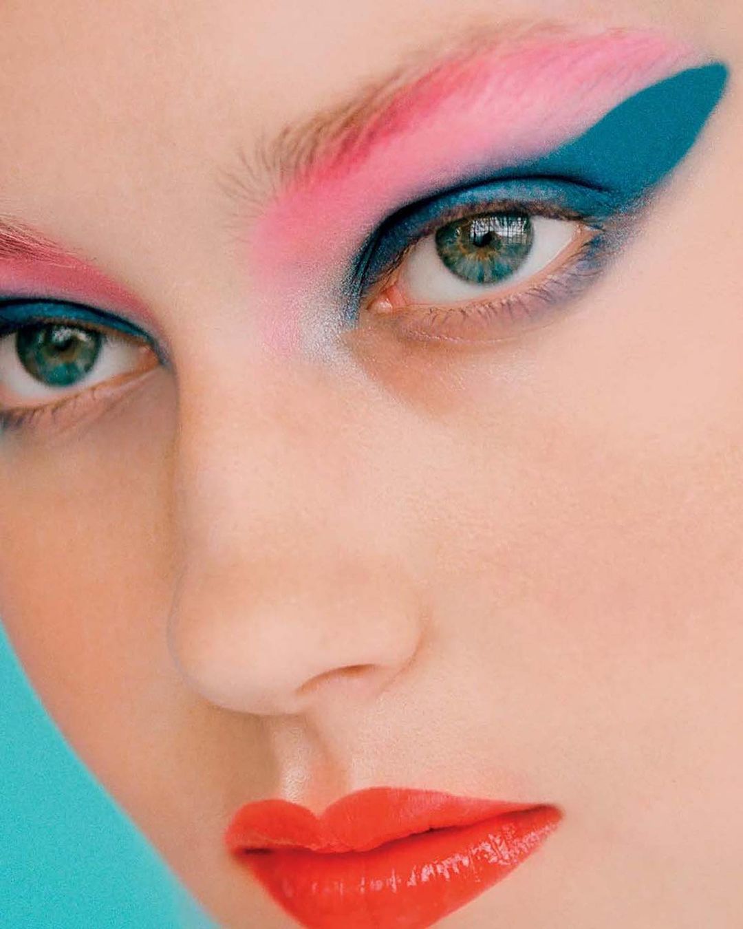 Close-up beauty portrait of a person with vivid pink eyebrows, teal eye shadow, and bright red lipstick captured by Dennis Stenild.