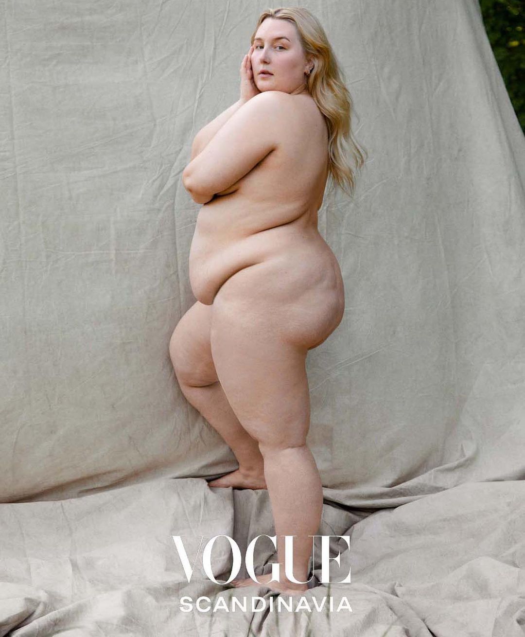 Full-body shot of a nude woman with blonde hair posing against a canvas backdrop, featuring the Vogue Scandinavia logo.