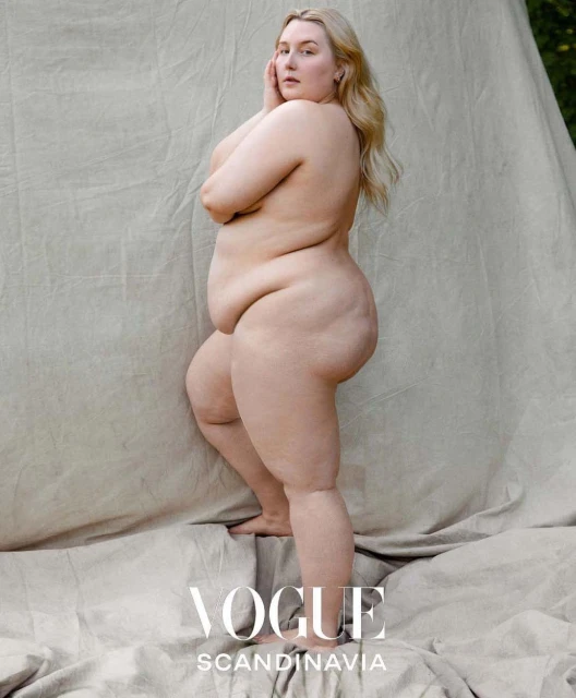 Full-body shot of a nude woman with blonde hair posing against a canvas backdrop, featuring the Vogue Scandinavia logo.