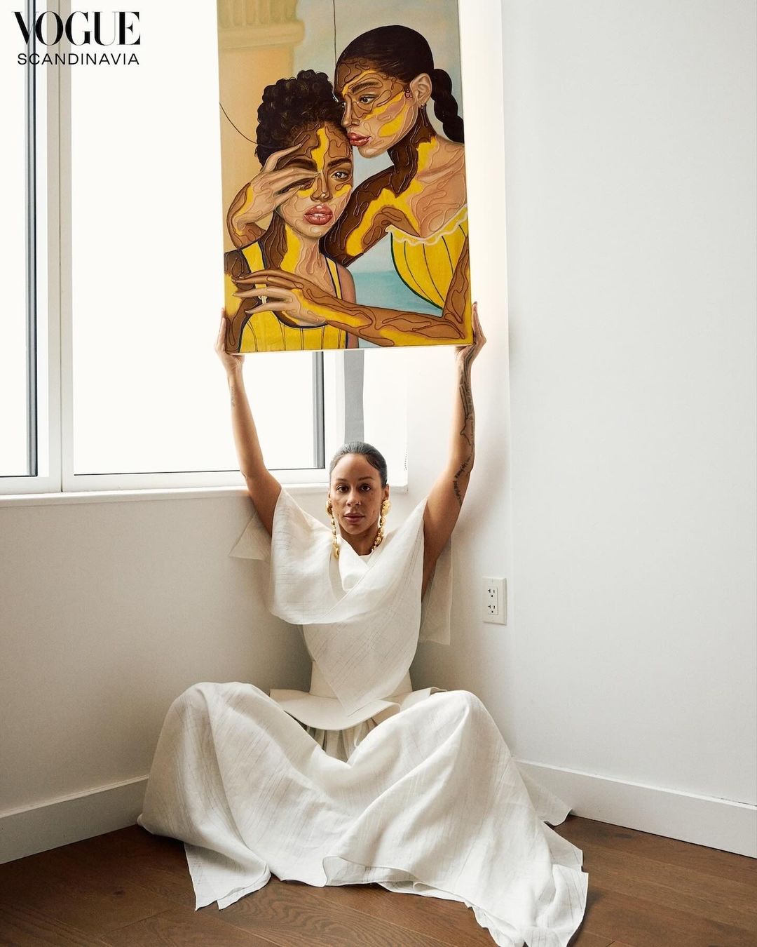 Woman in white dress sitting on the floor holding a framed painting above her head by photographer Dennis Stenild
