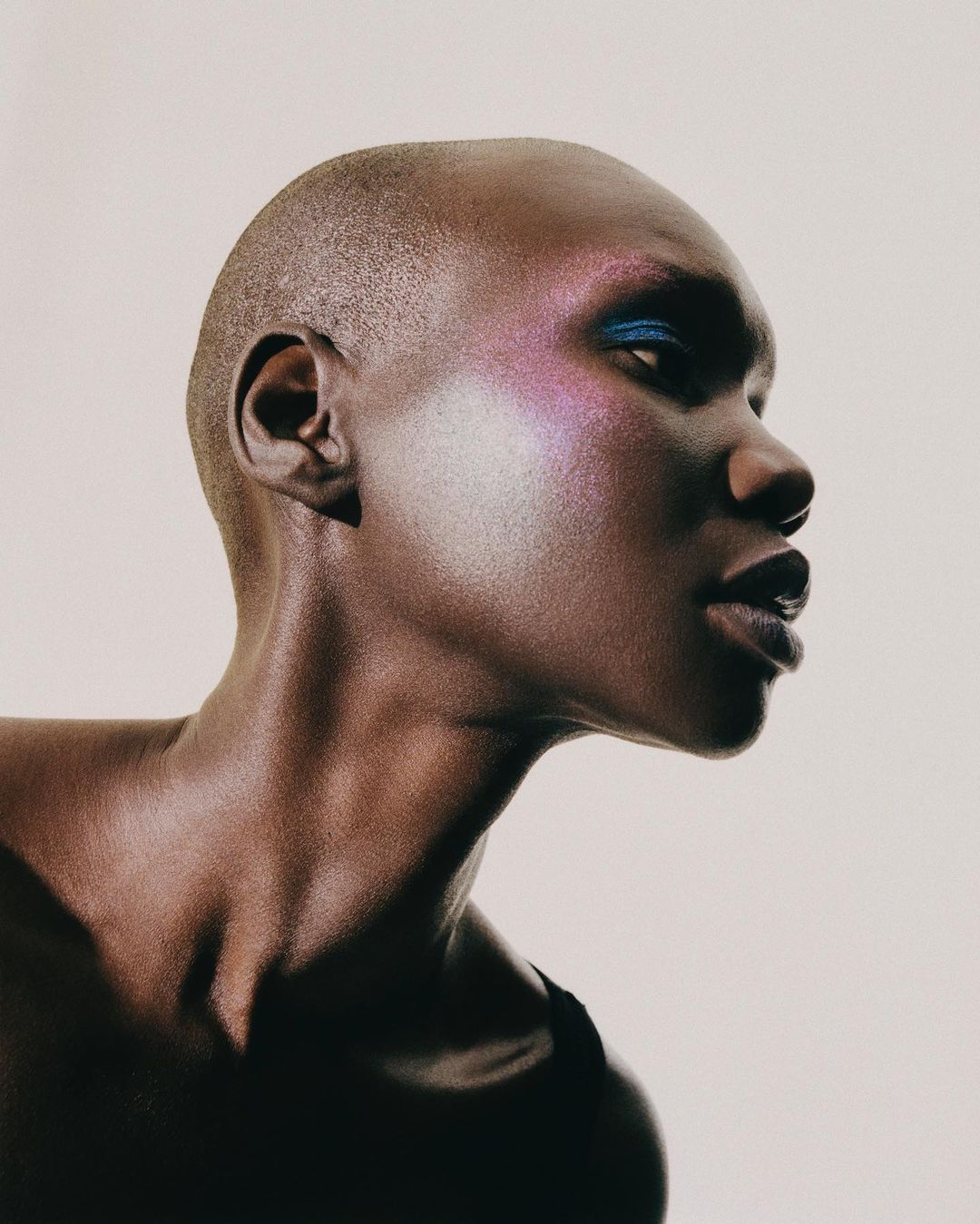 Close-up portrait of a bald African-American adult female model with dramatic eyeshadow and makeup, posing in a photo studio.