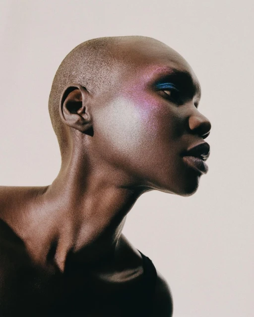 Close-up portrait of a bald African-American adult female model with dramatic eyeshadow and makeup, posing in a photo studio.