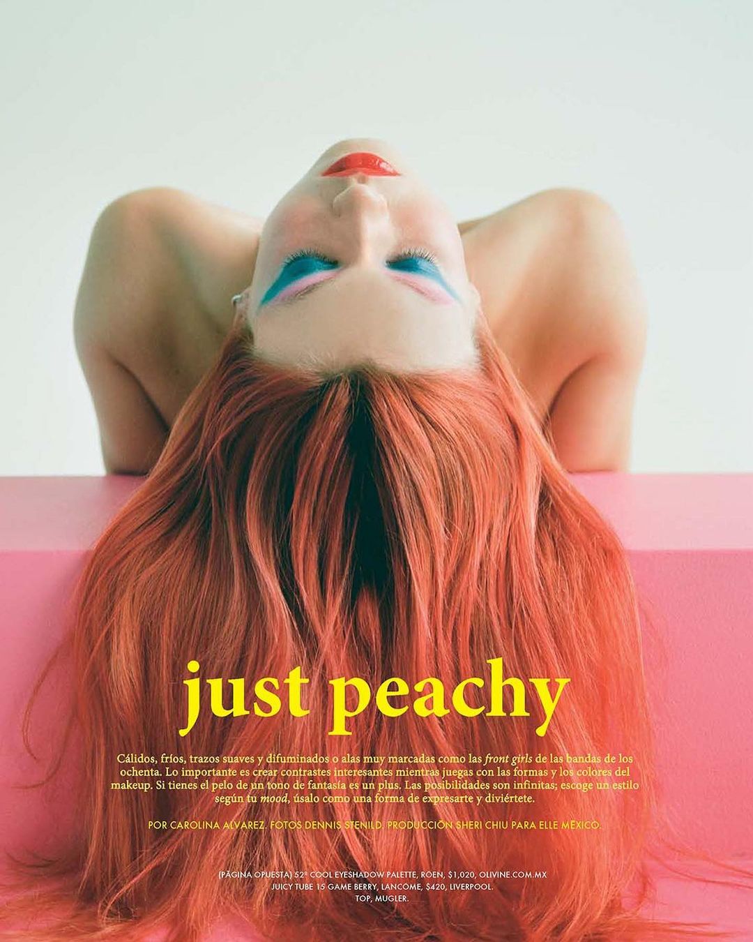 Woman with vibrant makeup and red hair lies on a pink surface, shot from overhead in a beauty editorial style against a white background.