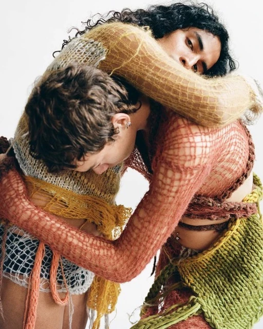 Two people embrace wearing knit garments in a fashion editorial featuring textured fabrics and neutral tones in a light, studio environment.