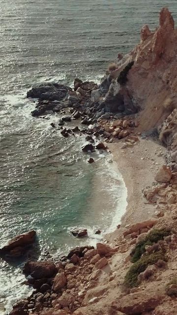 Scenic view of a secluded beach with clear turquoise water, rocky cliffs, and sandy shore under natural light.