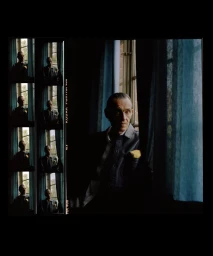 Portrait of an older man standing by a window with blue curtains, shot on analog film with contact sheet borders.